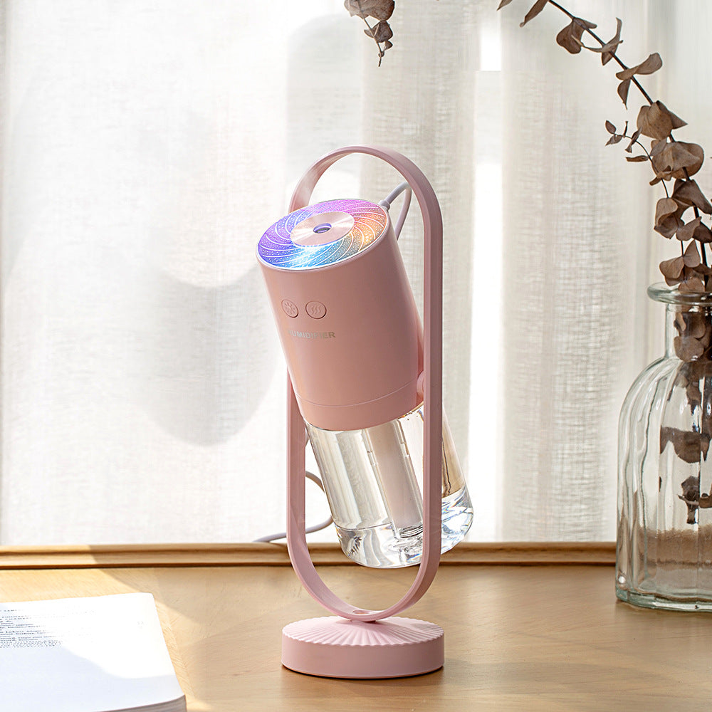Aurora projection humidifier in light blue on a white desk beside a laptop